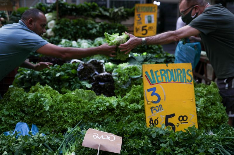 © Reuters. A man hands over a lettuce to another man as prices are displayed at a weekly street market in Rio de Janeiro, Brazil July 8, 2021. REUTERS/Amanda Perobelli