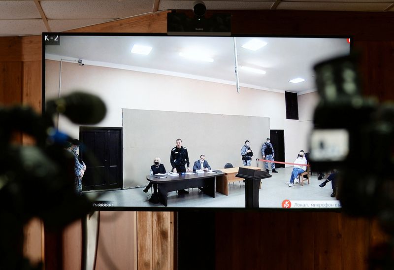 &copy; Reuters. Alexeï Navalny (debout) et ses avocats sur un écran lors d'une audience au centre correctionnel pour hommes IK-2, à Pokrov, dans la région de Vladimir. Le parquet russe a requis mardi une peine supplémentaire de 13 ans de prison contre l'opposant Ale