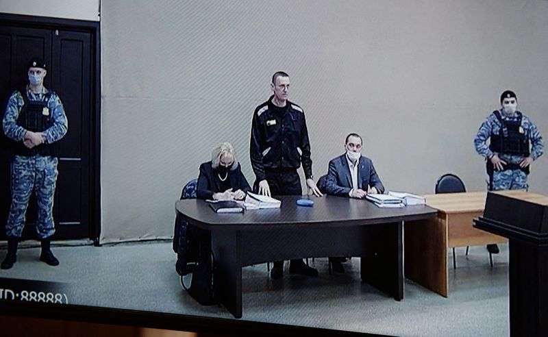 © Reuters. Alexeï Navalny (debout) et ses avocats sur un écran lors d'une audience au centre correctionnel pour hommes IK-2, à Pokrov, dans la région de Vladimir. Le parquet russe a requis mardi une peine supplémentaire de 13 ans de prison contre l'opposant Alexeï Navalny pour fraude et outrage à la justice. /Photo prise le 15 février 2022/REUTERS/Denis Kaminev