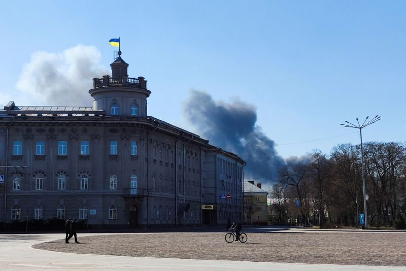 &copy; Reuters. Pessoas caminham na praça principal de Chernihiv, na Ucrânia, enquanto fumaça sobe ao fundo depois de disparos de artilharia
14/03/2022 REUTERS/Oleh Holovatenko