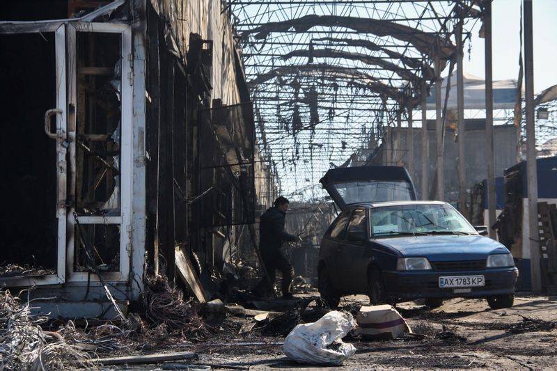 © Reuters. A man walks next to a car at a damaged market Barabashovo after a fire caused by shelling, as Russia's invasion of Ukraine continues, in Kharkiv, Ukraine March 19, 2022. REUTERS/Oleksandr Lapshyn