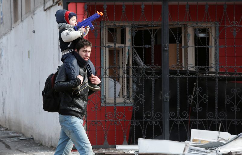 © Reuters. A child sits on the shoulders of a man near a building damaged during Ukraine-Russia conflict in the besieged southern port city of Mariupol, Ukraine March 20, 2022. REUTERS/Alexander Ermochenko