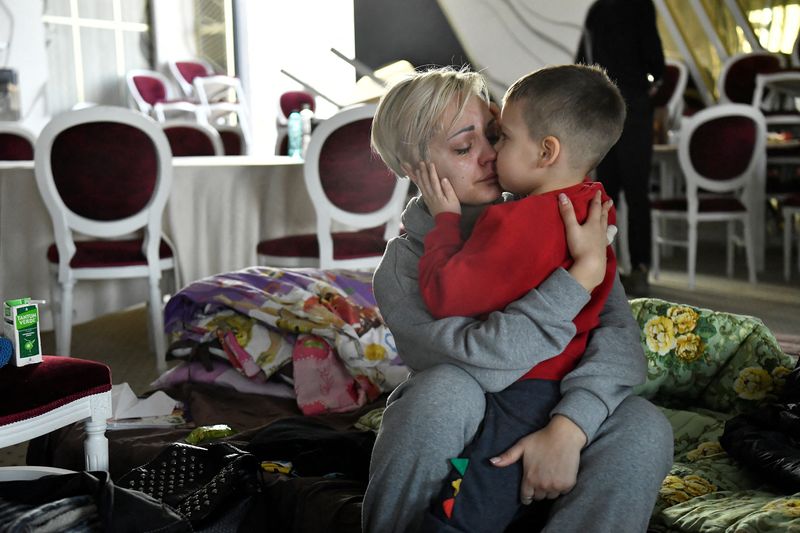 © Reuters. Egor, 5, comforts his mother Helen Yakubets who cries in a ballroom, which has been converted to a temporary shelter, at the Mandachi hotel after fleeing from Chernihiv in Ukraine to Romania, following Russia's invasion of Ukraine, at the border crossing in Suceava, Romania, March 20, 2022. Her 18 year old son and husband remain in Ukraine to fight. REUTERS/Clodagh Kilcoyne 