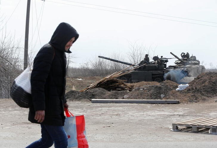 &copy; Reuters. Un hombre lleva sus pertenencias mientras pasa junto a varios tanques de tropas prorrusas a las afueras del asesidado puerto sureño de Mariúpol, Ucrania. 20 marzo 2022. REUTERS/Alexander Ermochenko