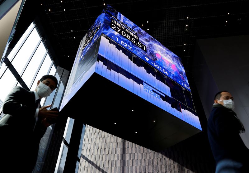 &copy; Reuters. FILE PHOTO: Men wearing protective face masks walk under an electronic board showing Japan’s Nikkei share average inside a conference hall, amid the coronavirus disease (COVID-19) pandemic, in Tokyo, Japan January 25, 2022.  REUTERS/Issei Kato