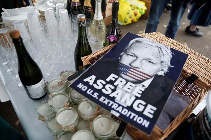 &copy; Reuters. Un cartel en el que se pide la liberación de Julian Assange y el bloqueo de su extradición junto a una imagen del periodista con la boca cubierta por una bandera de Estados Unidos, junto a botellas de vino espumoso, vasos, velas y otros objetos reunidos