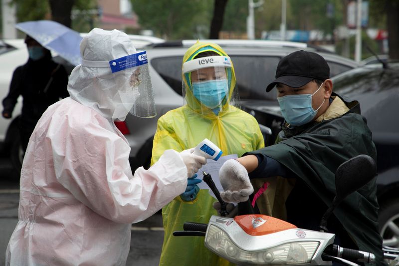 &copy; Reuters. FILE PHOTO: Volunteers in protective gear measure the body temperature of a man at the entrance of a residential compound following the coronavirus disease (COVID-19) outbreak, in Chuanying district of Jilin, Jilin province, China May 22, 2020. China Dail