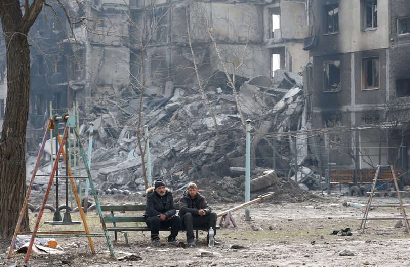 &copy; Reuters. Moradores sentam-se em um banco perto de um prédio de apartamentos destruído por bombardeios em Mariupol
25/03/2022
REUTERS/Alexander Ermochenko