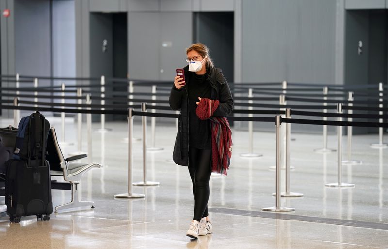 &copy; Reuters. FILE PHOTO: A passenger wearing a face mask looks at her phone beside an empty security queue at Dulles International Airport, a day after U.S. President Donald Trump announced travel restrictions on flights from Europe to the United States for 30 days to