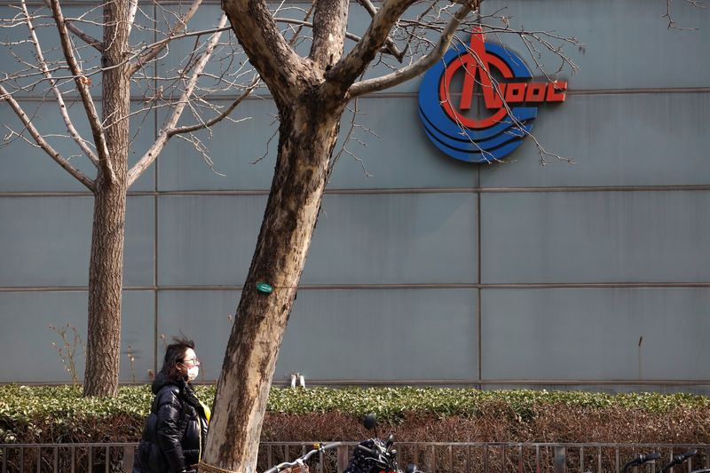 &copy; Reuters. FILE PHOTO: A woman wearing a face mask walks past a sign of China National Offshore Oil Corp (CNOOC) outside its headquarters in Beijing, China March 8, 2021. REUTERS/Tingshu Wang