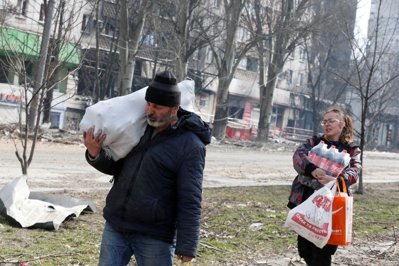 &copy; Reuters. Residentes locales llevan alimentos mientras pasan por delante de un edificio de apartamentos dañado durante el conflicto entre Ucrania y Rusia en la asediada ciudad portuaria del sur de Mariupol, Ucrania 31 de marzo de 2022. REUTERS/Alexander Ermochenko