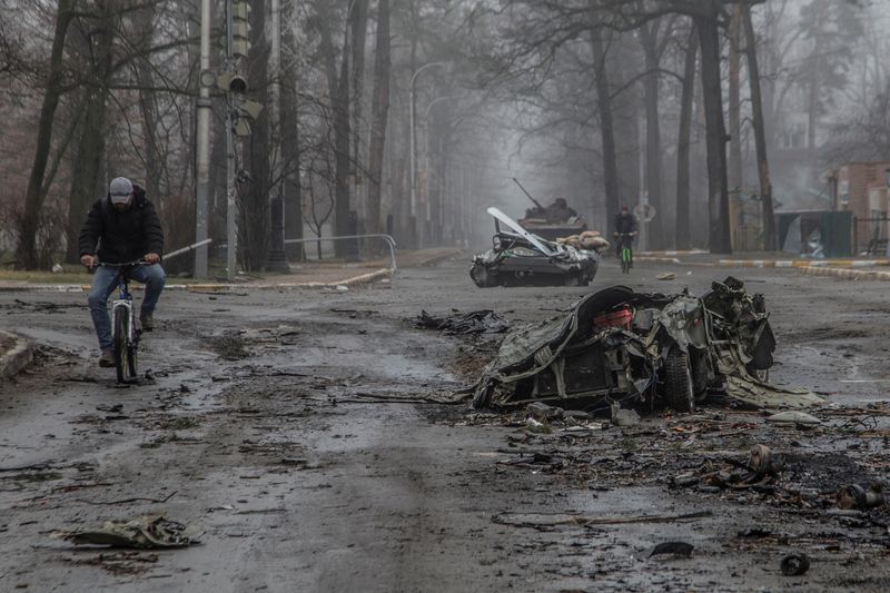 © Reuters. ساكنان محليان يركبان دراجاتهما بالقرب من سيارات مدنية مدمرة في بلدة بوتشا في العاصمة الأوكرانية كييف في الأول من أبريل نيسان 2022. تصوير: أولكسندر راتوشنياك-رويترز.