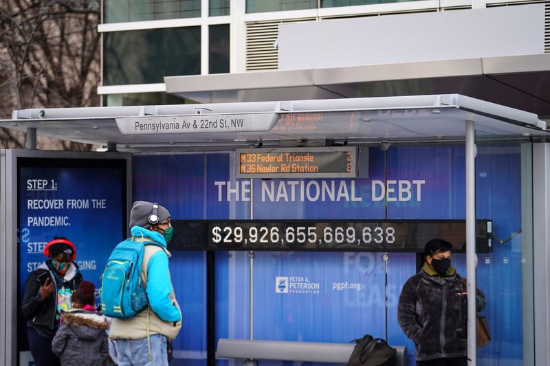 © Reuters. FILE PHOTO: People wearing protective face masks wait at a bus stop with a display of the current national debt amid the coronavirus disease (COVID-19) pandemic in Washington, U.S. January 31, 2022.  REUTERS/Sarah Silbiger