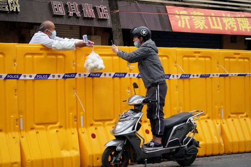 © Reuters. FILE PHOTO: A man standing on a scooter scans a QR code to buy food from a vendor behind barricades of a sealed-off area, following the coronavirus disease (COVID-19) outbreak in Shanghai, China March 30, 2022. REUTERS/Aly Song/File Photo