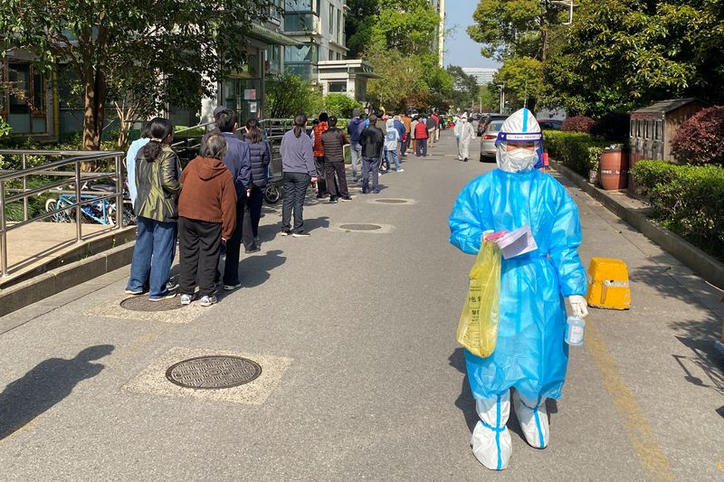 &copy; Reuters. FILE PHOTO: A medical worker in a protective suit walks past a line of people waiting to take nucleic acid test at a locked down residential area,  following the coronavirus disease (COVID-19) outbreak in Shanghai, China April 7, 2022. Picture taken April