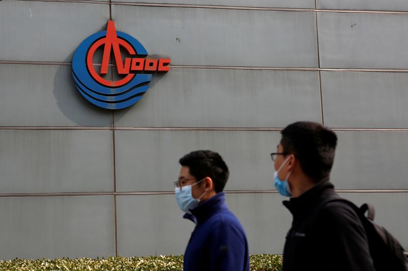 &copy; Reuters. FILE PHOTO: Men wearing face masks walk past a sign of China National Offshore Oil Corp (CNOOC) outside its headquarters in Beijing, China March 8, 2021. REUTERS/Tingshu Wang