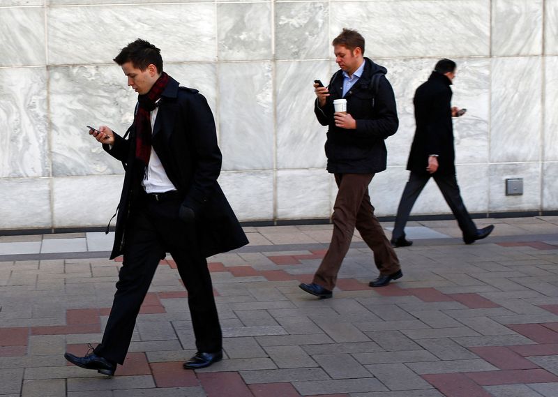 &copy; Reuters. FILE PHOTO: People look at their phones while walking at the Canary Wharf business district in London February 26, 2014. REUTERS/Eddie Keogh