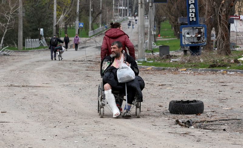 &copy; Reuters. Una mujer tira de una silla de ruedas en la que transporta a un hombre herido durante la invasión rusa de Ucrania en la ciudad de Mariúpol, Ucrania, el 18 de abril de 2022. REUTERS/Alexander Ermochenko