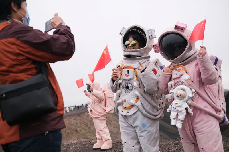 &copy; Reuters. FILE PHOTO: People dressed in astronaut costumes and holding flags of China pose for pictures while visiting the Volcano No. 6 of the Ulan Hada volcano group near Ulanqab, Inner Mongolia Autonomous Region, China October 4, 2021. REUTERS/Carlos Garcia Rawl