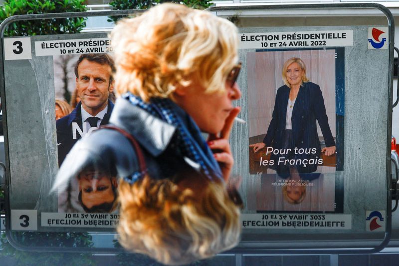 © Reuters. Una mujer pasa frente a pósters oficiales de los candidatos a la presidencia de Francia Marine le Pen y Emmanuel Macron en París, Francia, 19 de abril del 2022. REUTERS/Gonzalo Fuentes
