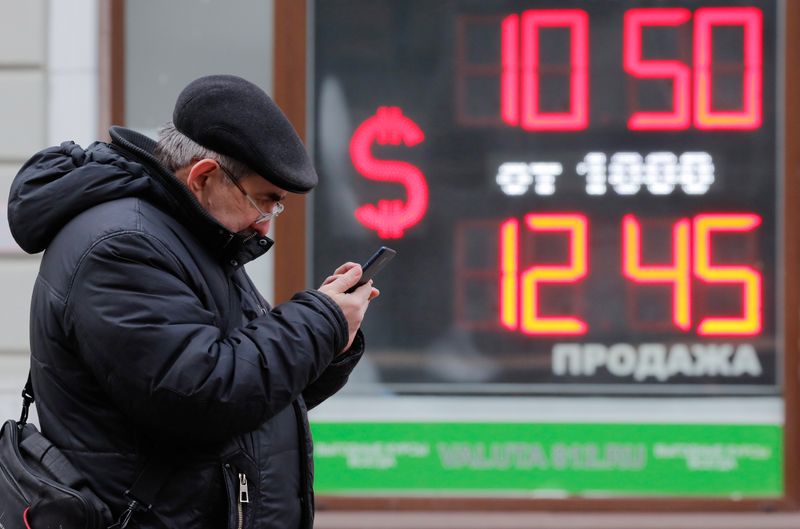 &copy; Reuters. FILE PHOTO: A man uses his smartphone near a board showing currency exchange rates of U.S. dollar against the Russian rouble in Saint Petersburg, Russia February 28, 2022. REUTERS/Anton Vaganov/File Photo