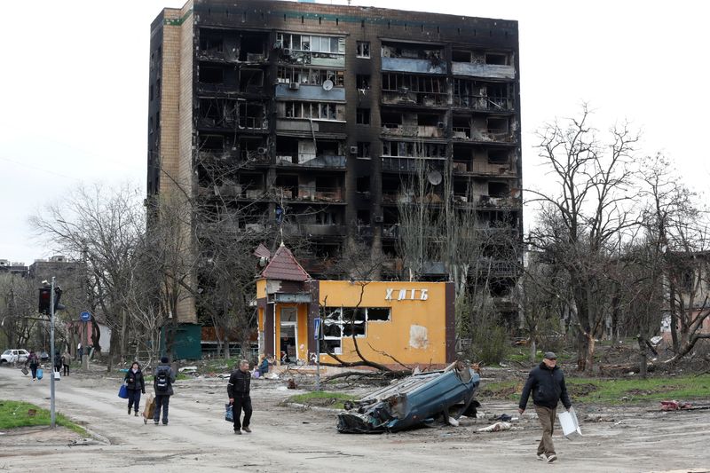 &copy; Reuters. Pessoas caminham em frente a prédio residencial fortemente danificado durante conflito entre Rússia e Ucrânia na cidade ucraniana de Mariupol
21/04/2022 REUTERS/Alexander Ermochenko