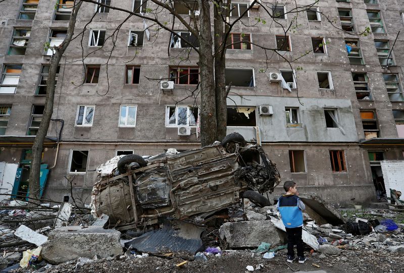 © Reuters. A boy stands next to a wrecked vehicle in front of an apartment building damaged during Ukraine-Russia conflict in the southern port city of Mariupol, Ukraine April 24, 2022. REUTERS/Alexander Ermochenko