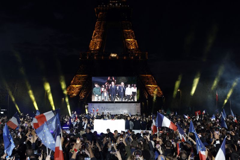 © Reuters. French President Emmanuel Macron is seen on screen as he arrives on stage with his wife, French first lady Brigitte Macron,  after being re-elected as president, following the results in the second round of the 2022 French presidential election, during his victory rally at the Champ de Mars in Paris, France, April 24, 2022. REUTERS/Gonzalo Fuentes