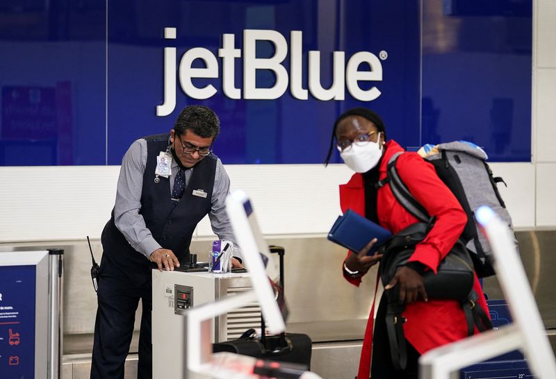 &copy; Reuters. FILE PHOTO: An unmasked JetBlue Airlines worker assists a masked traveler after the Biden administration announced it would no longer enforce a U.S. coronavirus disease (COVID-19) mask mandate on public transportation, following a federal judge's ruling t