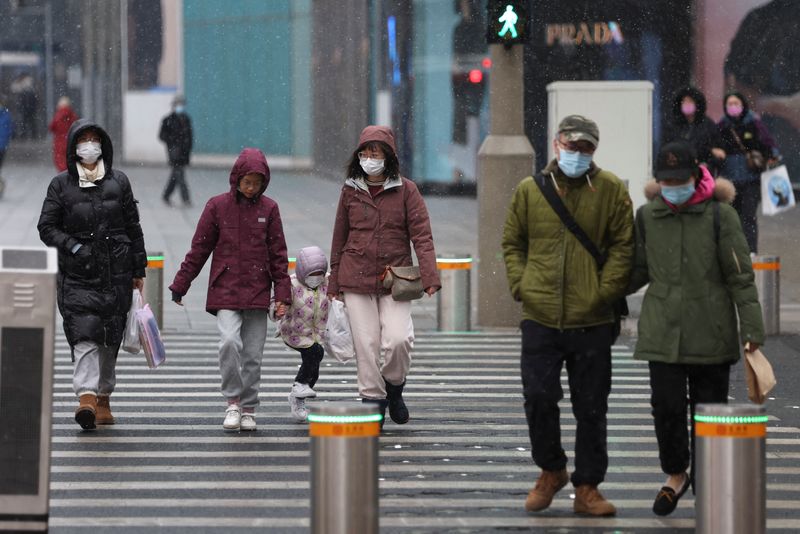 &copy; Reuters. FOTO DE ARCHIVO: Personas con mascarillas pasan por una calle en medio de una nevada, tras el brote de la enfermedad del coronavirus (COVID-19), en una zona comercial de Pekín, China, el 17 de marzo de 2022. REUTERS/Tingshu Wang