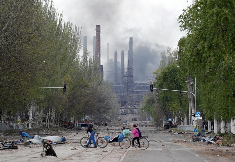 &copy; Reuters. مدنيون يعبرون طريقا مع دراجاتهم وفي الخلفية تتصاعد أعمدة الدخان من مصنع أزوفستال لأعمال الحديد والصلب خلال الحرب الدائرة بين أوكرانيا وروس
