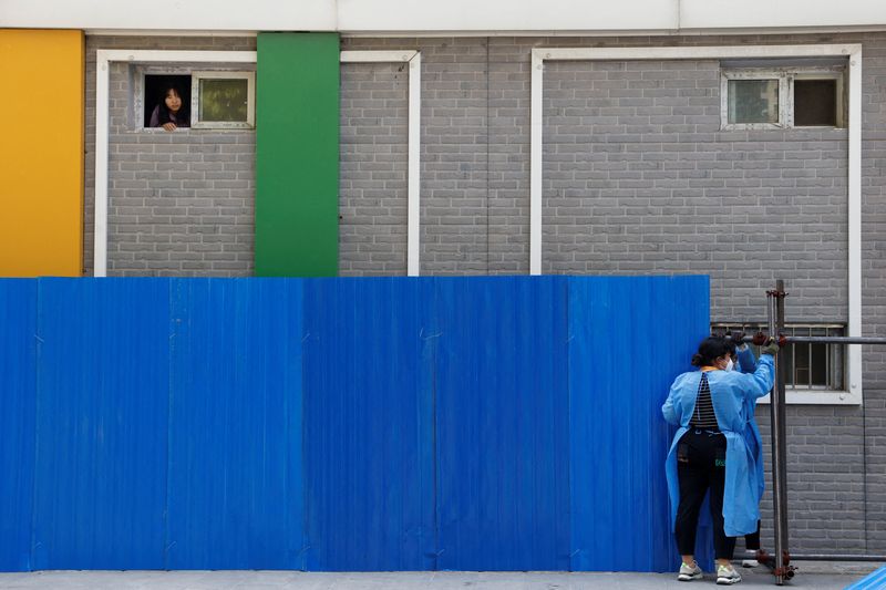 © Reuters. Workers wearing personal protective equipment (PPE), install a barricade around a residential area under lockdown while a resident looks out from a window, amid the coronavirus disease (COVID-19) outbreak in Beijing, China, May 4, 2022. REUTERS/Carlos Garcia Rawlins   