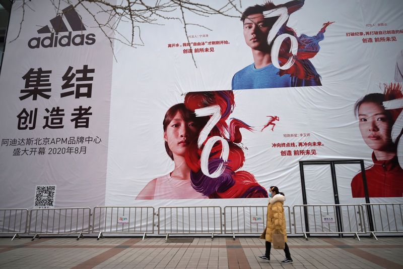 &copy; Reuters. A woman wearing a face mask walks past a banner advertising new Adidas store, as the country is hit by an outbreak of the novel coronavirus, in Beijing, China February 20, 2020. REUTERS/Tingshu Wang/Files