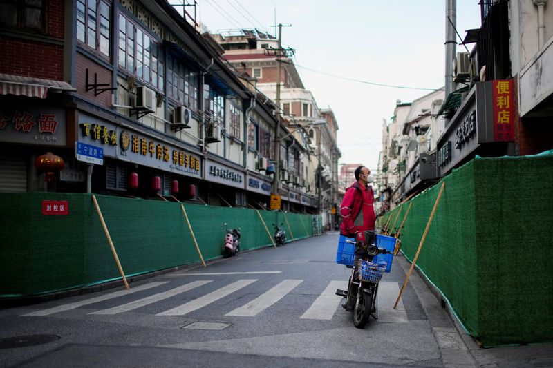 &copy; Reuters. Un repartidor a domicilio con mascarilla en una motocicleta mira por encima de una barrera que rodea un área residencial durante el confinamiento por la COVID-19 en Shanghái, China, el 9 de mayo de 2022. REUTERS/Aly Song