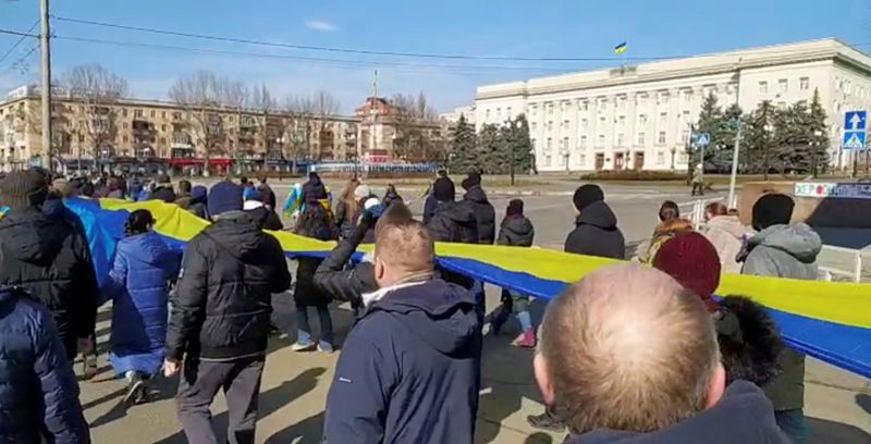 &copy; Reuters. FOTO DE ARCHIVO. Imágenes transmitidas en directo muestran a personas portando una pancarta con los colores de la bandera ucraniana mientras protestan en medio de la invasión rusa de Ucrania, en Jersón, Ucrania. 13 de marzo de 2022, en esta imagen fija
