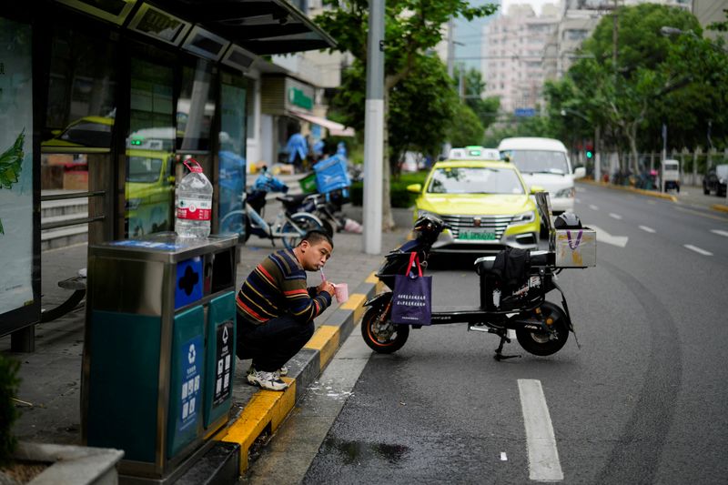 &copy; Reuters. A delivery worker, who says he is living at a bus stop because he has been unable to return home for weeks due to the lockdown, brushes his teeth on a street, amid the coronavirus disease (COVID-19) pandemic, in Shanghai, China, May 12, 2022. REUTERS/Aly 