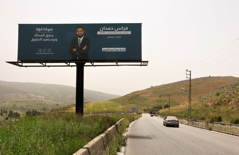 &copy; Reuters. A car passes near an electoral campaign billboard depicting Firas Hamdan, a lawyer who is running as an opposition candidate in Lebanon's parliamentary election, in Kfar Tebnit village, southern Lebanon, April 30, 2022. Picture taken April 30, 2022. REUTE