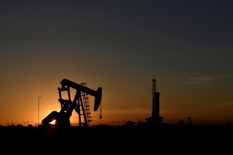 &copy; Reuters. Imagen de archivo de un balancín operando frente a una plataforma de perforación durante una puesta de sol en un campo petrolero en Midland
