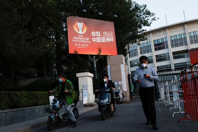 &copy; Reuters. FOTO DE ARCHIVO: Hombres con mascarillas pasan junto a un cartel publicitario de la Copa Asiática, al salir de un lugar de prueba de ácido nucleico improvisado durante el brote de COVID-19 en Pekín, China, 14 de mayo de 2022. REUTERS/Carlos García Raw