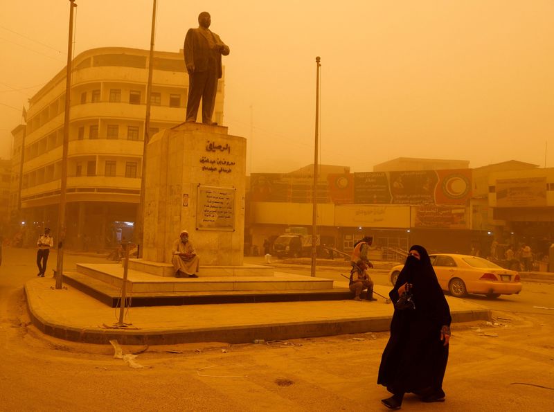 &copy; Reuters. امرأة تمشي بجوار تمثال للشاعر العراقي عبد الغني معروف الرصافي أثناء عاصفة رملية في العاصمة بغداد يوم الاثنين. تصوير: أحمد سعد رويترز.