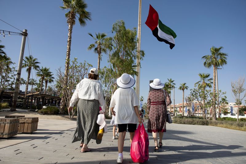 © Reuters. سائحون يسيرون بجانب علم دولة الإمارات في دبي يوم 13 مايو أيار 2022. تصوير:  كريستوفر بايك - رويترز. 