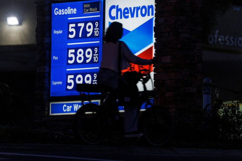 &copy; Reuters. FILE PHOTO: A woman rides an electric bike past a gas station as current gasoline prices continues to climb close to record setting territory in Encinitas, California, U.S., May 9, 2022.  REUTERS/Mike Blake