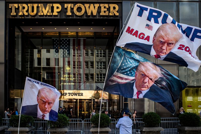&copy; Reuters. أحد مؤيدي الرئيس الأمريكي السابق دونالد ترامب يضع أعلاما تحمل صورته أمام برج ترامب في مدينة نيويورك يوم الأحد. تصوير: ديفيد ديلجادو - رويترز.