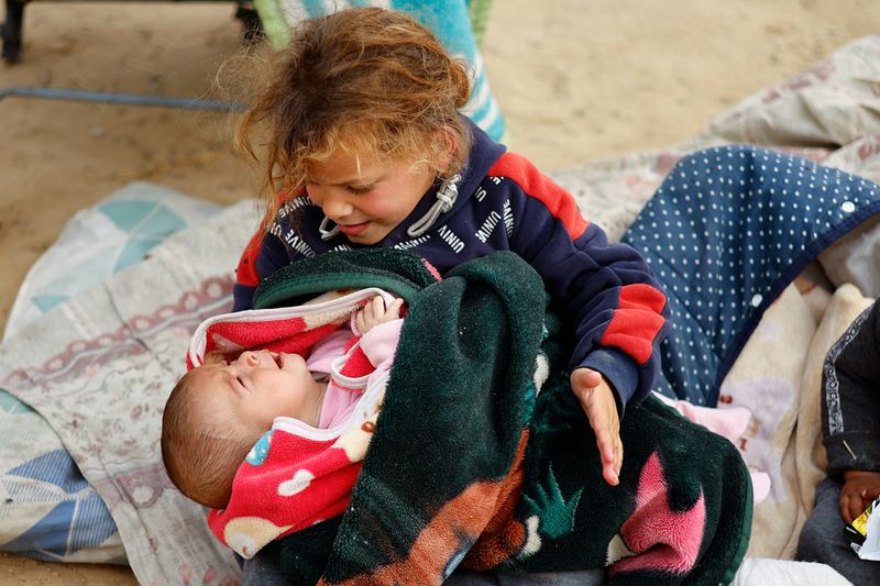 &copy; Reuters. Una niña palestina desplazada debido a los ataques israelíes sosteniendo a un bebé llorando, mientras se refugian en un campamento de tiendas de campaña en medio del conflicto entre Israel y Hamás, en Ráfah, sur de la Franja de Gaza. 13 de febrero d