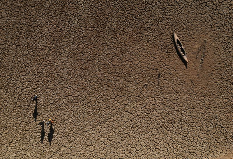 © Reuters. FILE PHOTO: Residents walk past a canoe sitting on cracked ground at a Sau reservoir, as the Iberian peninsula is at its driest in 1,200 years, in Sant Roma De Sau, Spain, January 31, 2024. REUTERS/Nacho Doce/File Photo