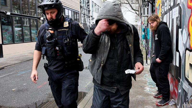 © Reuters. Police officer David Baer pulls a man, who was caught smoking fentanyl, to issue him a citation and to offer him a card that lists a 24-hour treatment hotline which he can call to get his citation dismissed in Portland, Oregon, U.S. February 7, 2024.  REUTERS/Deborah Bloom