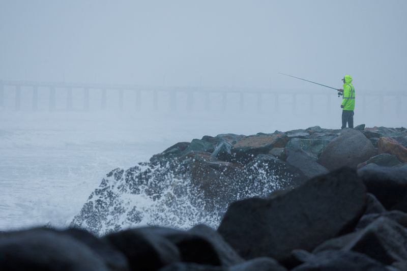 © Reuters. A man fishes off a rockwall beach break during a winter storm in Oceanside, California, U.S., February 20, 2024.  REUTERS/Mike Blake