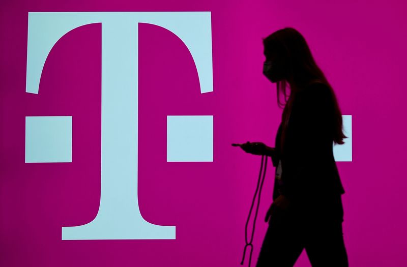 &copy; Reuters. FILE PHOTO: A woman carrying her phone passes by the logo of German telecommunication company "Deutsche Telekom" at the ITS World Congress 2021, a fair for intelligent transport systems, in Hamburg, Germany, October 13, 2021. REUTERS/Fabian Bimmer/File Ph