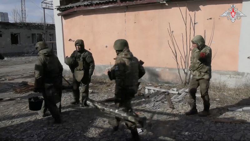 &copy; Reuters. أفراد من الجيش الروسي يسيرون بالقرب من مبنى تعرض لدمار في موقع تم تحديده على أنه أفدييفكا بأوكرانيا في صورة مأخوذة من مقطع فيديو متداول على 