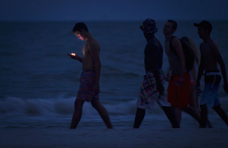 © Reuters. FILE PHOTO: A person looks at his cell phone as he and others walk along the beach at twilight during the Labour Day long weekend in Ft Myers Beach, Florida August 31, 2014. REUTERS/Carlo Allegri/File Photo